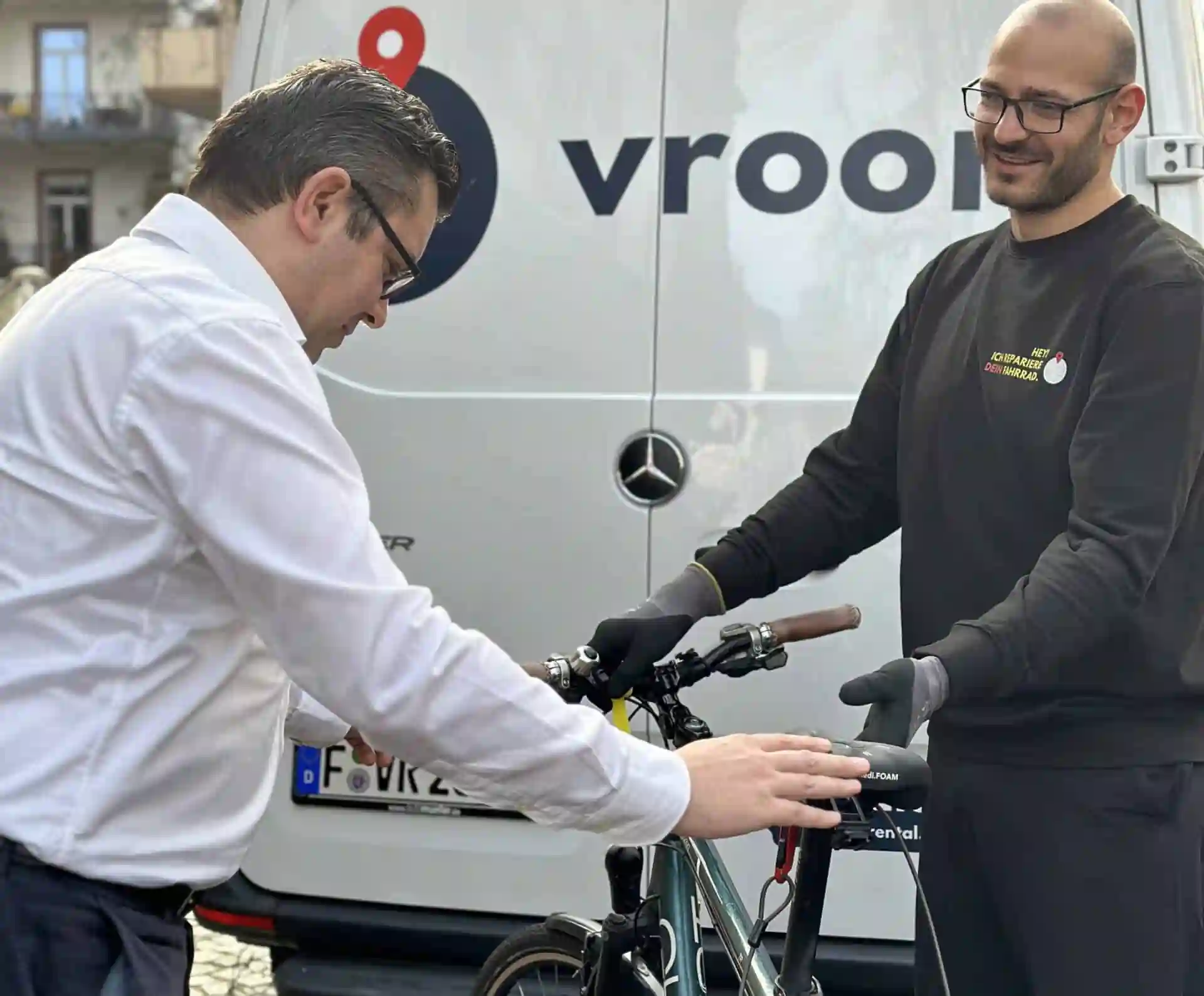 Ein Lieferfahrer von VROOM REPAIR übergibt das reparierte Fahrrad an den Kunden.
